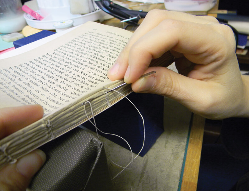 hands repairing a book with needle and thread
