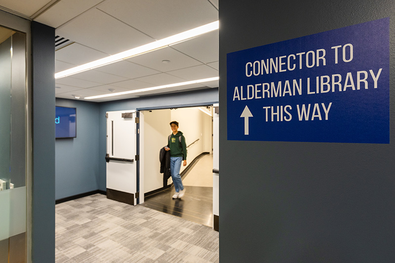 A person walks through an interior tunnel connecting two buildings. A sign in the foreground says “Connector to Alderman Library this way.”
