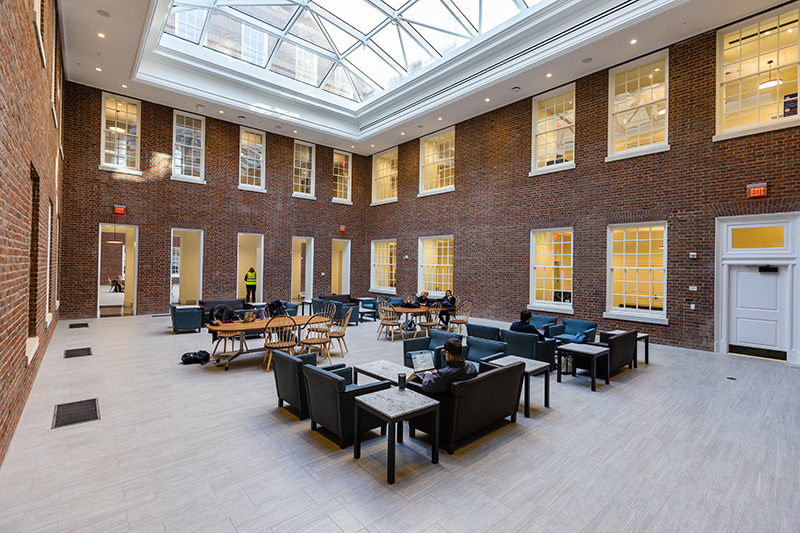 A courtyard showing brick walls and a mixture of wooden tables and chairs and soft seating, under a skylight.