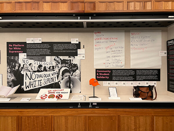 A display case shows a photo of a crowd holding protest signs such as ‘No dialogue with white supremacy’ while one person speaks into a megaphone. Also visible are sheets of paper from planning sessions listing things like ‘plan of action,’ ‘buddy system,’ and ‘debrief interview.’ 