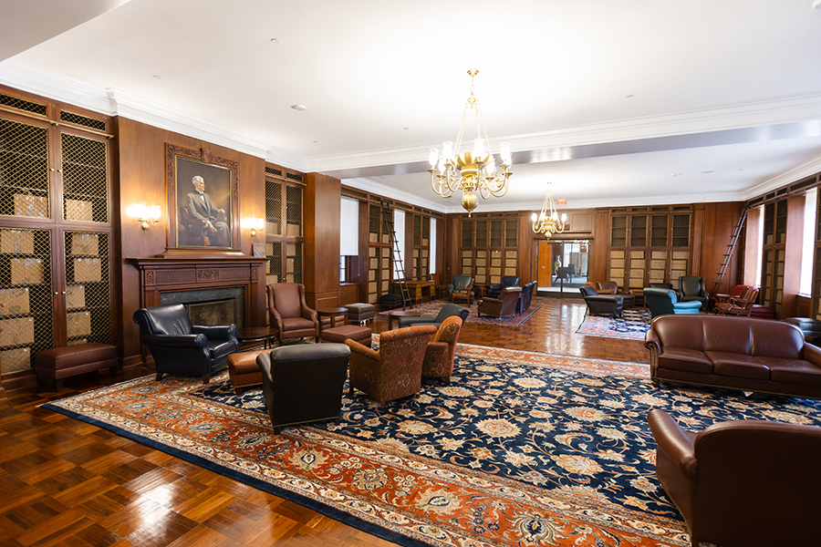 A large, luxurious room with a fireplace and bookshelves, filled with leather-bound furniture.