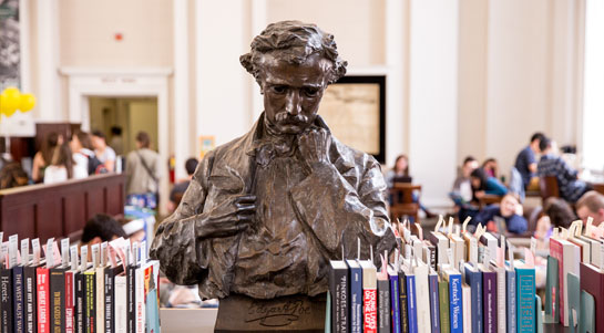 a bust of Edgar Allen Poe as it sits among books stacked on edge to either side