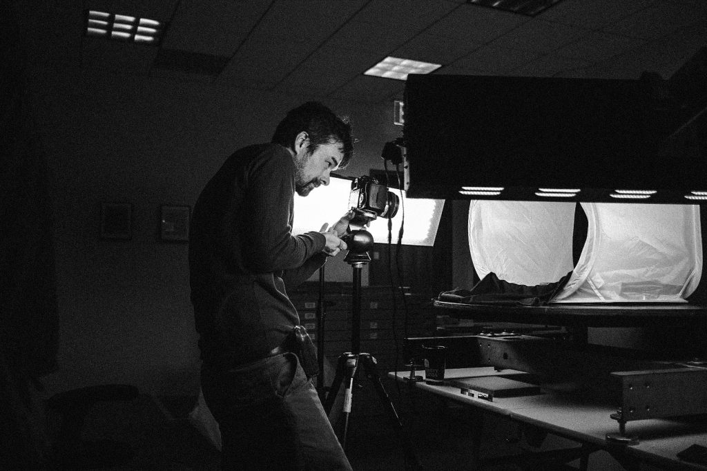 Black and white photo of a man adjusting a camera in a room filled with lighting equipment